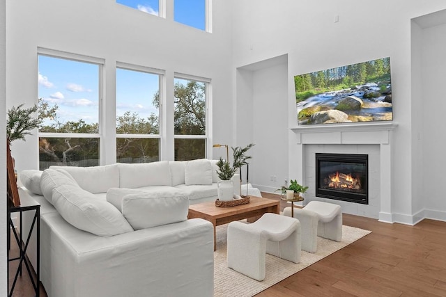 living room with wood-type flooring, a tile fireplace, a high ceiling, and plenty of natural light