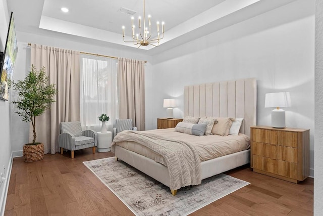 bedroom with a chandelier, light wood-type flooring, and a tray ceiling