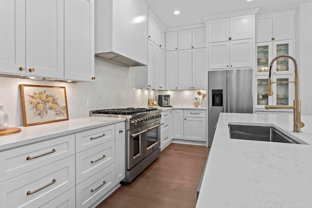 kitchen with dark wood finished floors, appliances with stainless steel finishes, white cabinets, a sink, and premium range hood