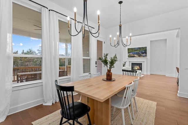 dining space featuring a notable chandelier, wood finished floors, a glass covered fireplace, and baseboards