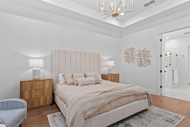 bedroom with connected bathroom, hardwood / wood-style floors, an inviting chandelier, and a tray ceiling