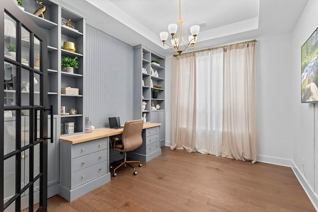 office space with a tray ceiling, a chandelier, and light wood-type flooring