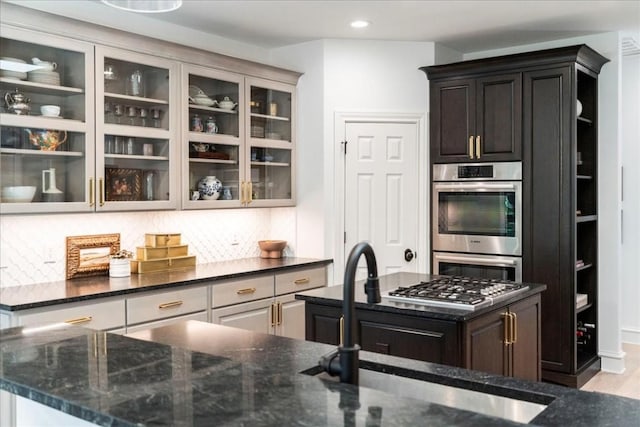 kitchen with a kitchen island, double oven, tasteful backsplash, sink, and dark stone counters