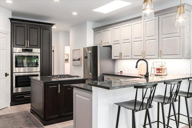 kitchen with a kitchen island, appliances with stainless steel finishes, backsplash, dark stone counters, and light wood-type flooring