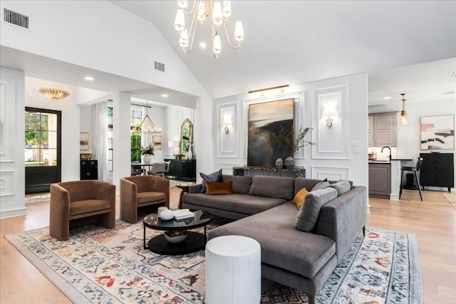 living room featuring high vaulted ceiling, sink, a notable chandelier, and light wood-type flooring