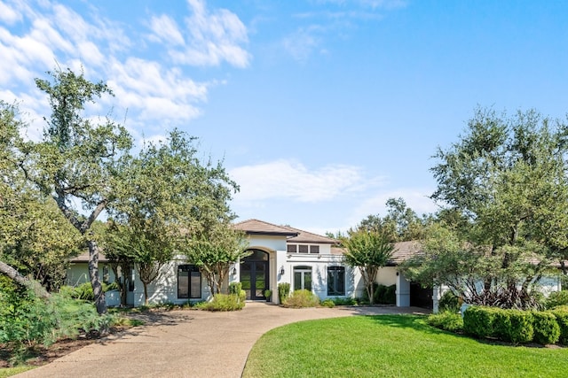 mediterranean / spanish home with a front lawn, a garage, stucco siding, french doors, and driveway