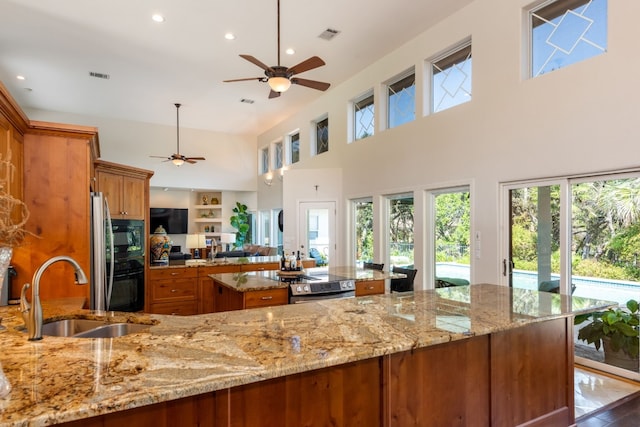 kitchen with sink, hanging light fixtures, a high ceiling, light stone counters, and black appliances