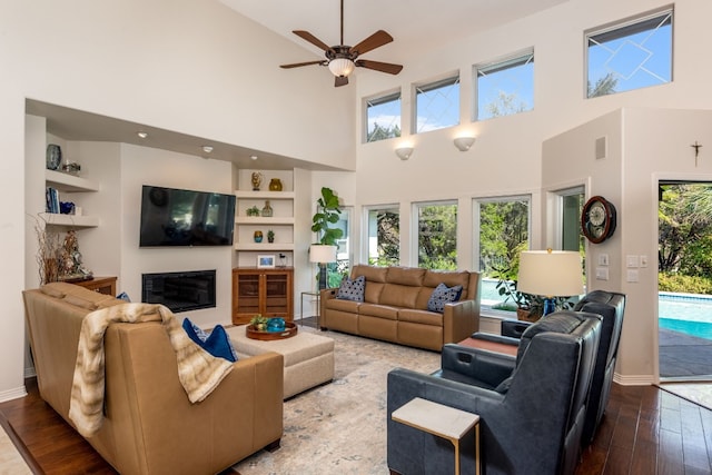 living room with ceiling fan, wood-type flooring, and a towering ceiling