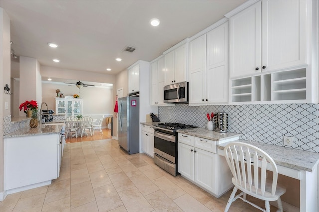 kitchen featuring white cabinetry, backsplash, light stone counters, kitchen peninsula, and stainless steel appliances