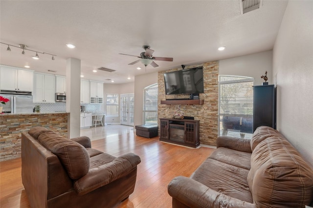 living room with ceiling fan, a stone fireplace, a textured ceiling, and light wood-type flooring