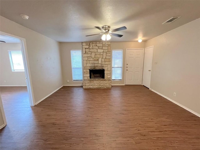 unfurnished living room with dark hardwood / wood-style flooring, a stone fireplace, and ceiling fan