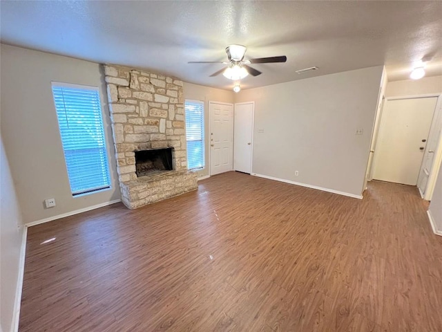 unfurnished living room with hardwood / wood-style flooring, ceiling fan, and a stone fireplace