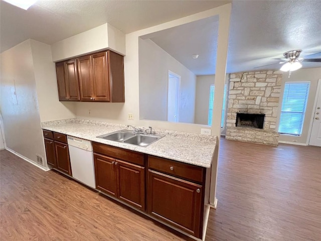 kitchen with white dishwasher, light hardwood / wood-style floors, sink, and a stone fireplace