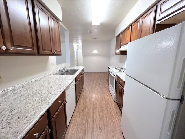 kitchen with sink, hanging light fixtures, light stone counters, white appliances, and light hardwood / wood-style flooring