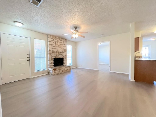 unfurnished living room featuring a wealth of natural light, a fireplace, light hardwood / wood-style floors, and ceiling fan