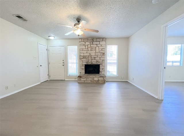 unfurnished living room featuring hardwood / wood-style floors, a stone fireplace, a textured ceiling, and ceiling fan