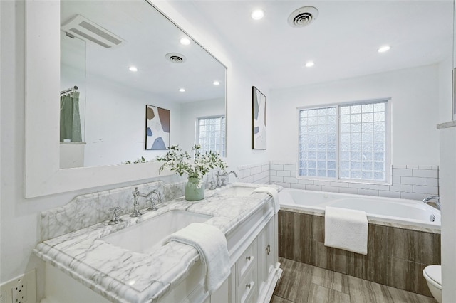 bathroom with vanity, toilet, and tiled bath