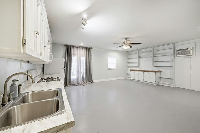 kitchen featuring concrete flooring, a wall mounted air conditioner, sink, white cabinets, and range