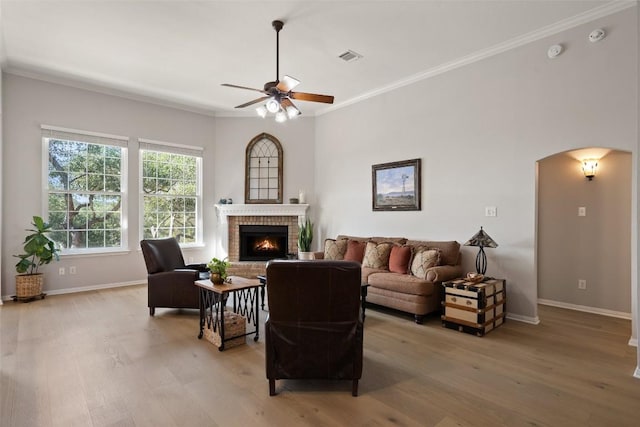 living room with ceiling fan, light hardwood / wood-style flooring, crown molding, and a fireplace