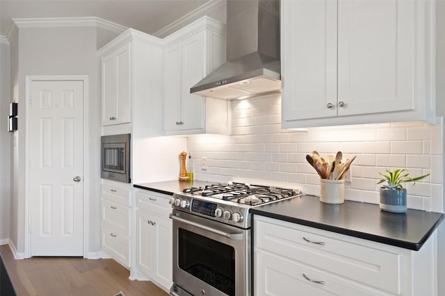 kitchen featuring wall chimney range hood, light hardwood / wood-style flooring, appliances with stainless steel finishes, white cabinetry, and decorative backsplash