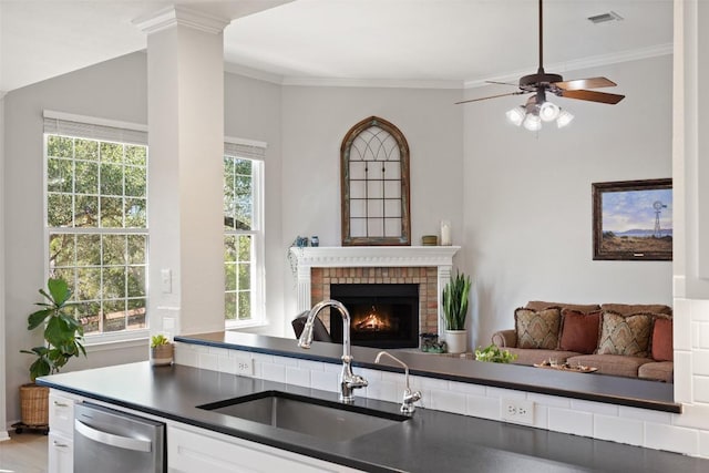 kitchen with sink, crown molding, a brick fireplace, stainless steel dishwasher, and ceiling fan