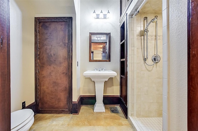 bathroom featuring a tile shower, tile patterned floors, and toilet