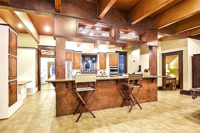 kitchen featuring beam ceiling, a breakfast bar, double oven, and kitchen peninsula