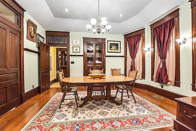 dining room featuring a chandelier, a raised ceiling, and light hardwood / wood-style floors