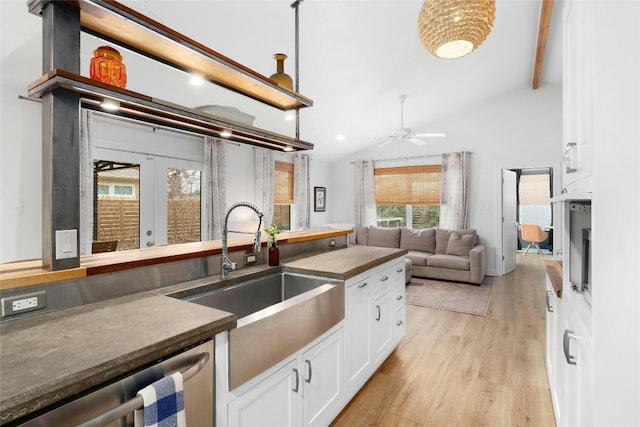 kitchen with sink, vaulted ceiling with beams, light wood-type flooring, stainless steel dishwasher, and white cabinets