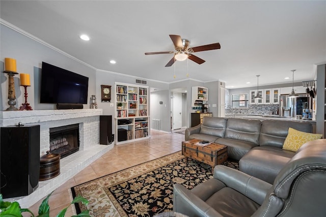 tiled living room with crown molding, ceiling fan, and a brick fireplace