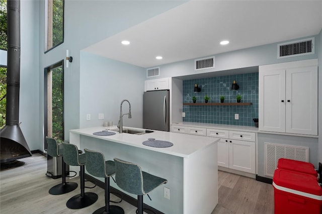 kitchen featuring stainless steel refrigerator, white cabinetry, sink, a kitchen bar, and light hardwood / wood-style flooring