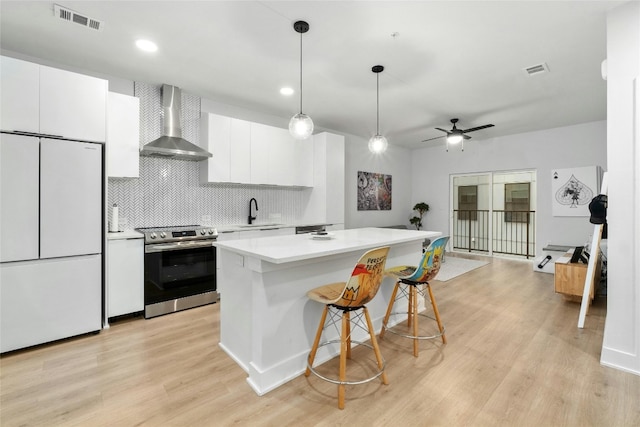 kitchen with stainless steel electric range, white cabinets, a kitchen island, built in fridge, and wall chimney exhaust hood