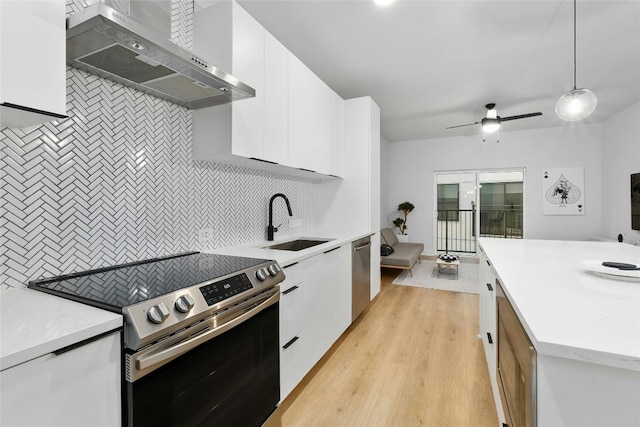 kitchen featuring sink, decorative light fixtures, appliances with stainless steel finishes, wall chimney range hood, and white cabinets