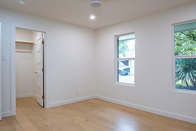 unfurnished bedroom featuring multiple windows, a spacious closet, light hardwood / wood-style floors, and a closet