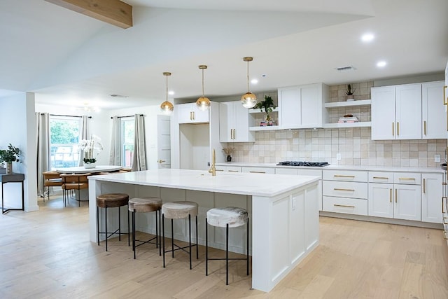 kitchen featuring decorative light fixtures, an island with sink, and white cabinets