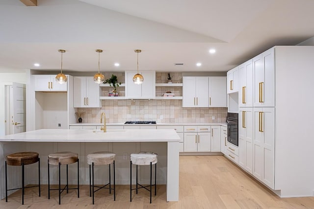 kitchen with a breakfast bar, sink, a center island with sink, black oven, and white cabinets