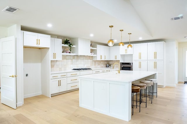 kitchen featuring decorative light fixtures, tasteful backsplash, white cabinets, a kitchen island with sink, and stainless steel oven