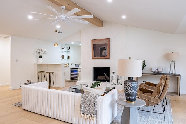 living room with ceiling fan, lofted ceiling with beams, bar area, beverage cooler, and light wood-type flooring