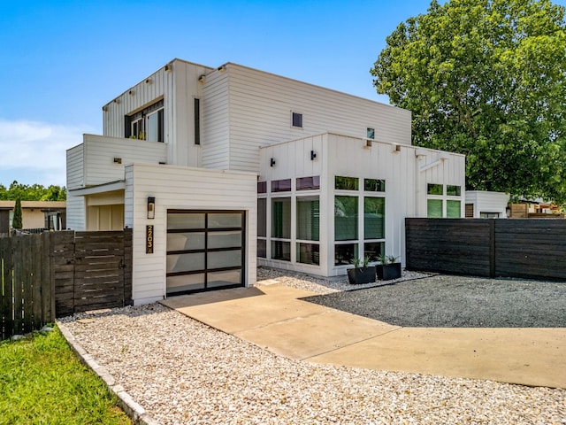 view of front facade featuring a garage, driveway, board and batten siding, and fence