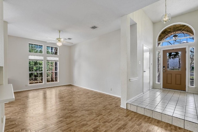 entryway featuring wood-type flooring, a towering ceiling, and ceiling fan with notable chandelier