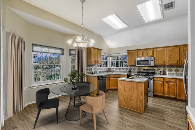 kitchen with wood-type flooring, decorative light fixtures, a kitchen island, stainless steel appliances, and decorative backsplash