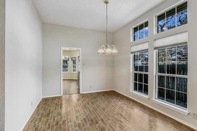 unfurnished dining area featuring wood-type flooring, a textured ceiling, and an inviting chandelier