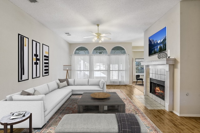 living room featuring ceiling fan, wood-type flooring, a tile fireplace, and a textured ceiling