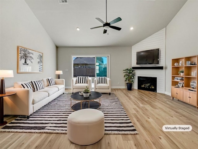 living room with ceiling fan, a large fireplace, vaulted ceiling, and light hardwood / wood-style flooring