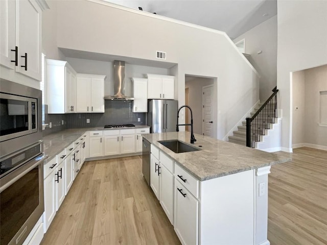17401 Howdy Way, Manor, TX 78653 - kitchen featuring appliances with stainless steel finishes, wall chimney range hood, a sink, light wood-style floors, and tasteful backsplash