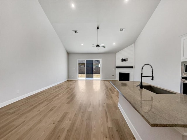 17401 Howdy Way, Manor, TX 78653 - unfurnished living room with a sink, a fireplace, ceiling fan, light wood-style flooring, and vaulted ceiling