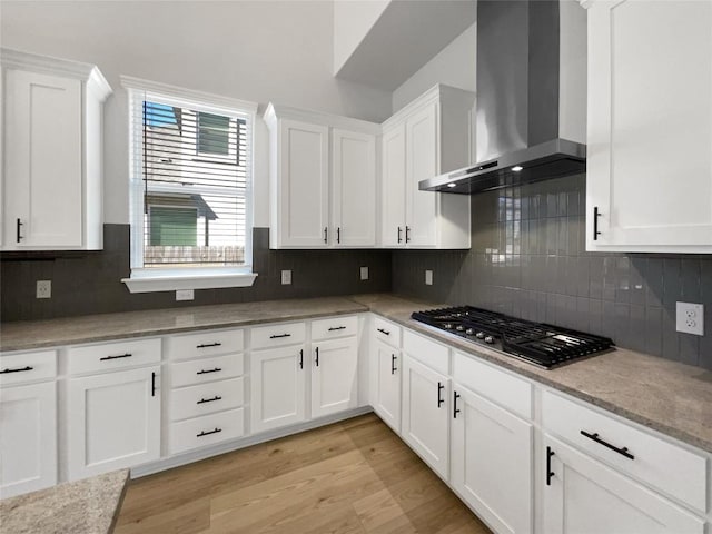 17401 Howdy Way, Manor, TX 78653 - kitchen with wall chimney range hood, stainless steel gas stovetop, white cabinets, light wood finished floors, and tasteful backsplash