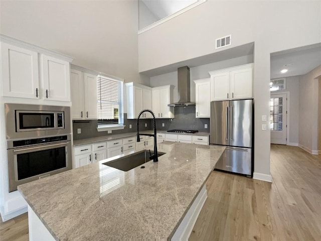 17401 Howdy Way, Manor, TX 78653 - kitchen with appliances with stainless steel finishes, wall chimney exhaust hood, a sink, light wood-style floors, and a towering ceiling