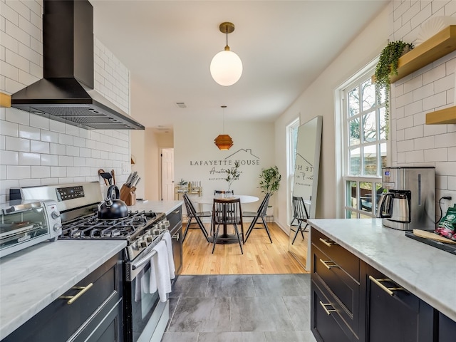 kitchen featuring decorative light fixtures, ventilation hood, backsplash, light stone counters, and stainless steel gas range