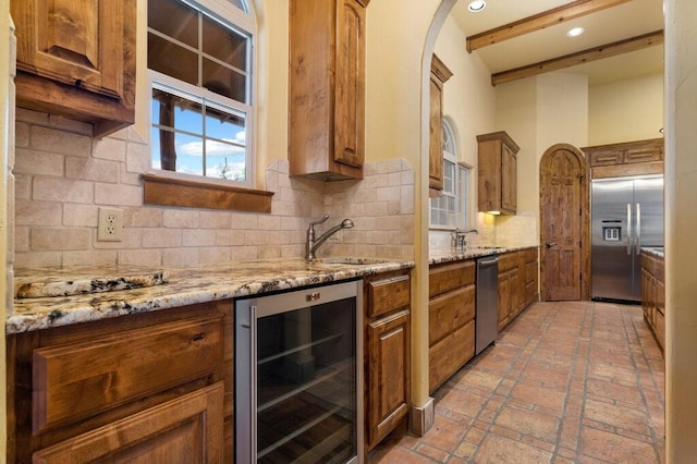 kitchen with sink, wine cooler, decorative backsplash, stainless steel appliances, and light stone countertops